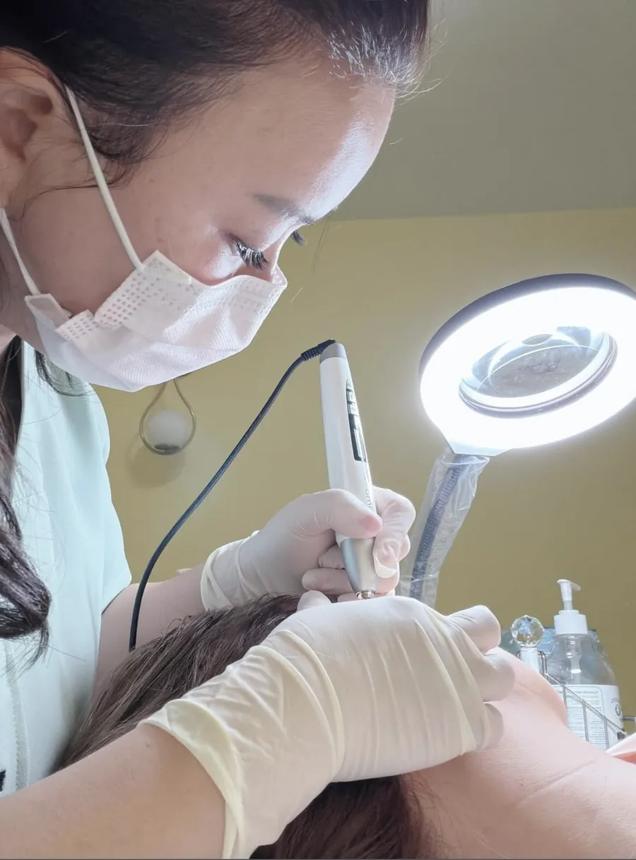 Esthetician performing a professional skin treatment under a magnifying lamp at The Beauty Story Skincare